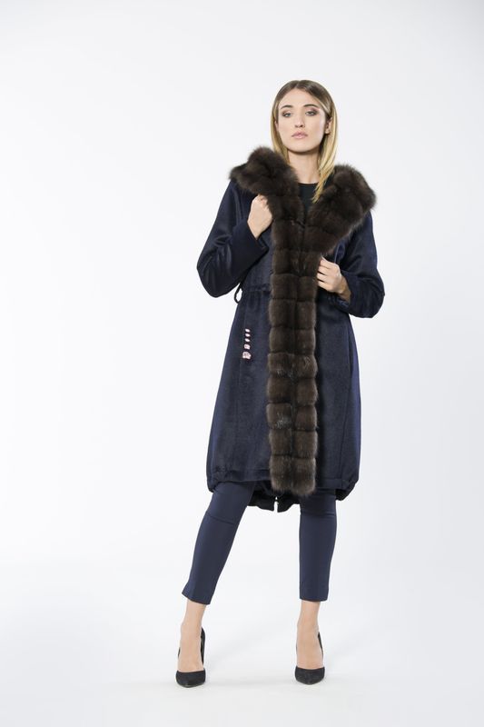 Woman in navy coat with brown fur trim, posing in front of a white background.