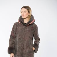 Woman in a long, brown hooded coat with fur cuffs and a pink trim, standing against a white backdrop.