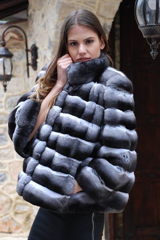 Woman wearing a short, gray and white fur jacket, standing outside, touching the jacket collar.
