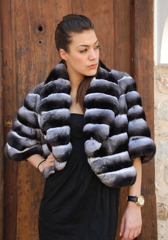 Woman wearing a short, fur bolero jacket over a black dress; standing in front of a wooden door.