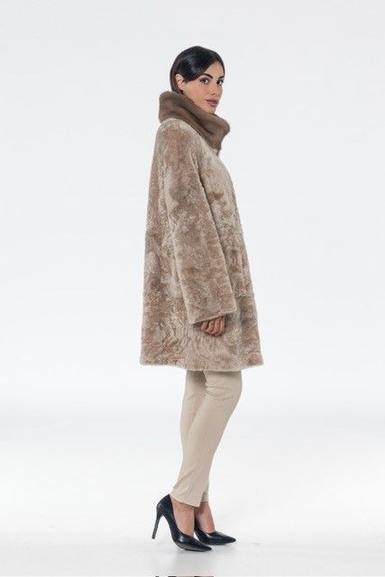 Woman in beige coat, standing, high collar, heels, light pants.