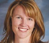 A headshot of a smiling person with shoulder-length blonde hair against a mottled blue background.