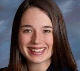 A smiling person with long brown hair, positioned in front of a blue, mottled background.