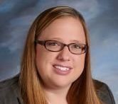 A person with shoulder-length brown hair and glasses, smiling, against a blue, textured background.