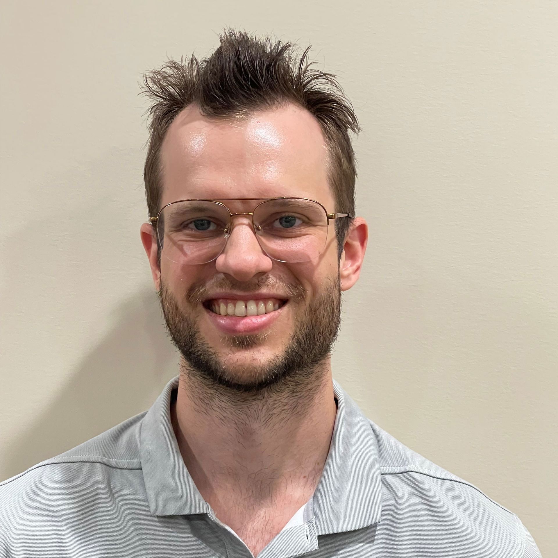 A person with short brown hair and a beard, wearing wire-rimmed glasses and a striped polo shirt, smiling at the camera.