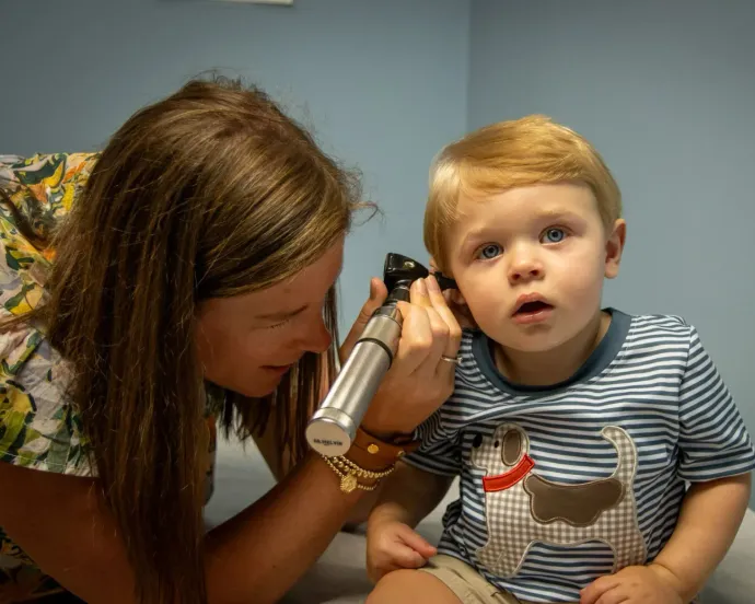 A healthcare professional uses an otoscope to examine the ear of a young child during a clinical appointment.