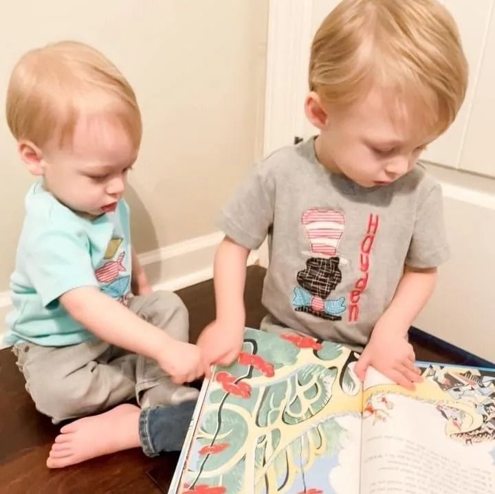 Two children sitting on the floor, pointing at a page in an open Dr. Seuss picture book.
