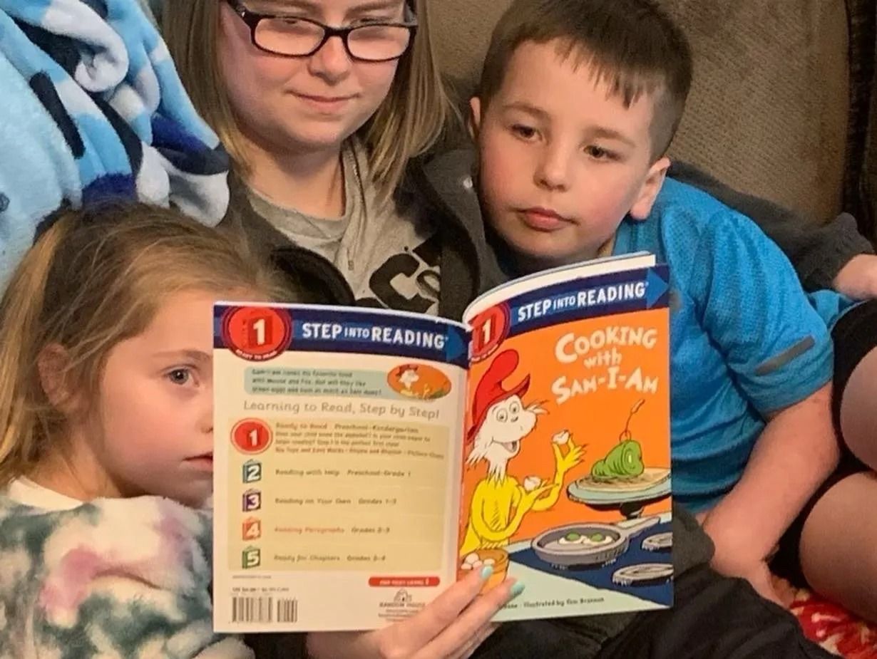 An adult and two children sit together while reading a 