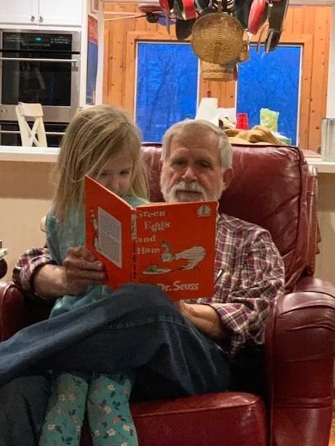 An adult and a child sit in a red leather chair, reading a Dr. Seuss book together in a kitchen setting.