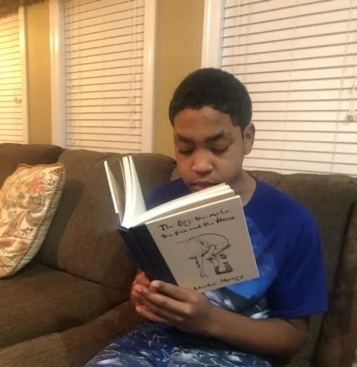 A person sits on a brown sofa reading a book titled 