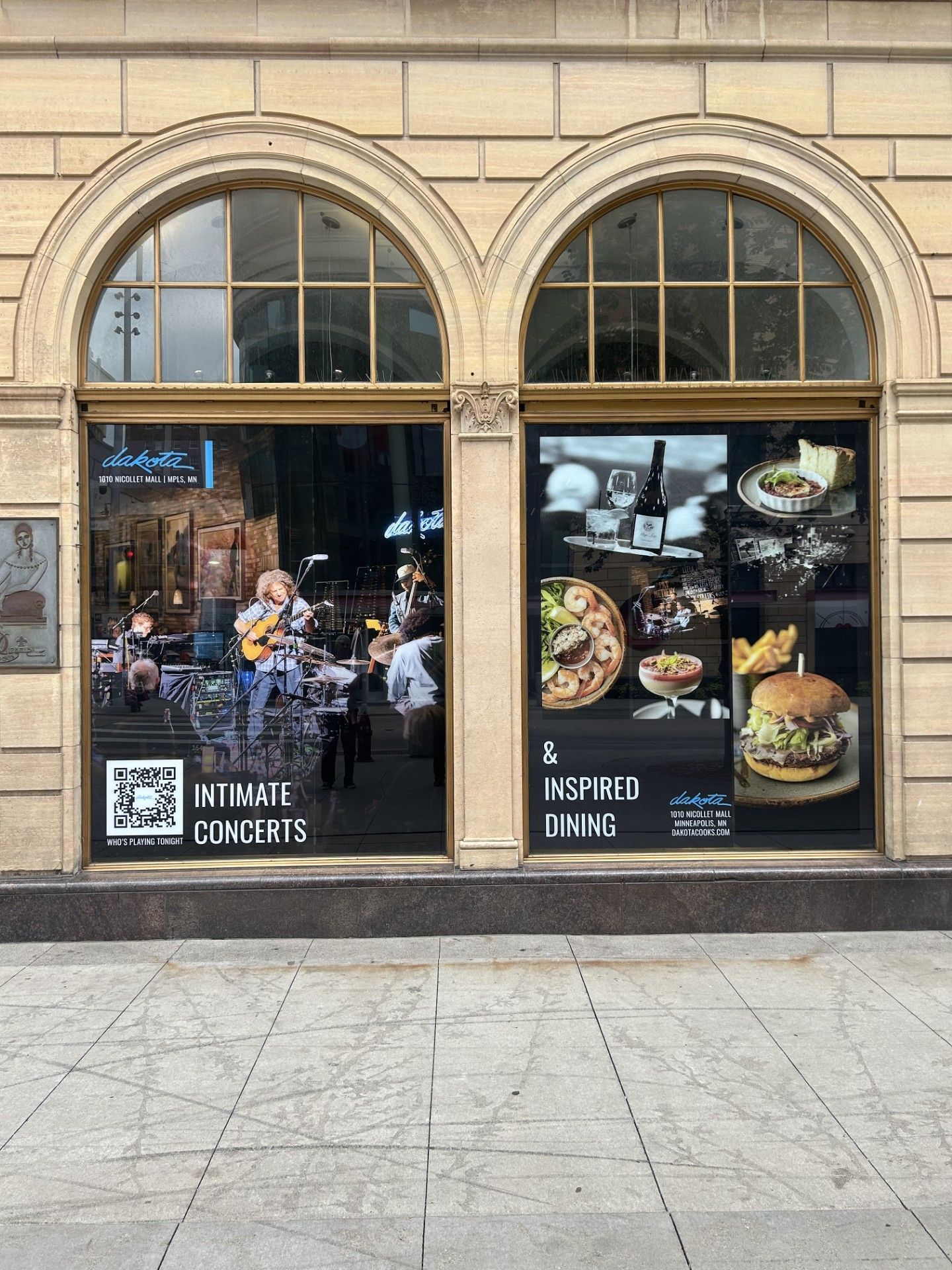 Arched storefront windows with a coffee shop display and an “Intimate Concerts” sign on a city sidewalk