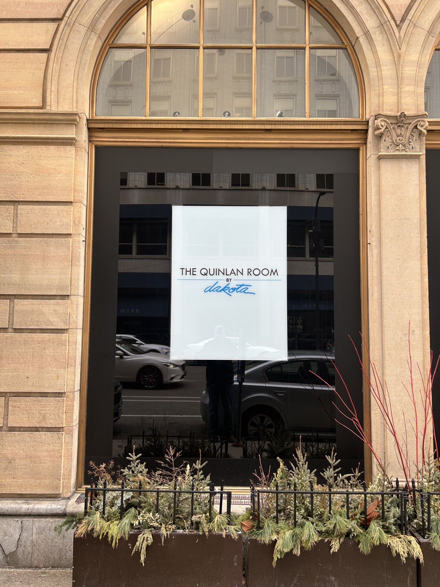 Storefront window with a white sign reading “The Quinlan Room” beneath an arched stone facade.