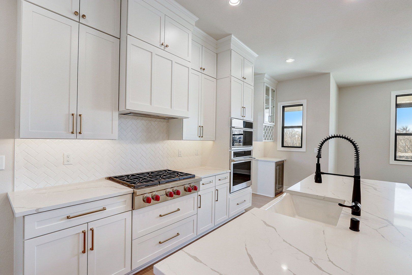 A kitchen with white cabinets , a stove , a sink , and a window.