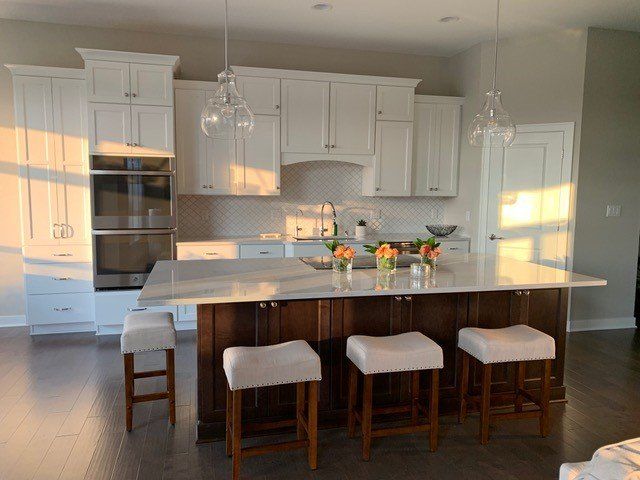 A kitchen with white cabinets and stools and a large island.