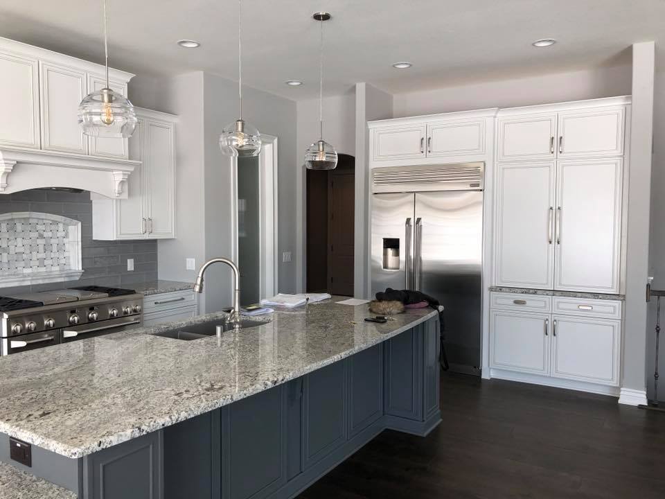 A kitchen with white cabinets , granite counter tops , stainless steel appliances and a large island.
