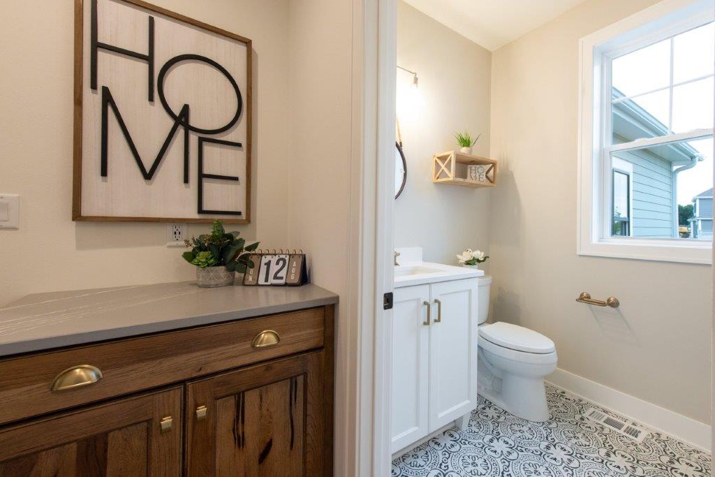 A bathroom with a toilet , sink , cabinets and a window.