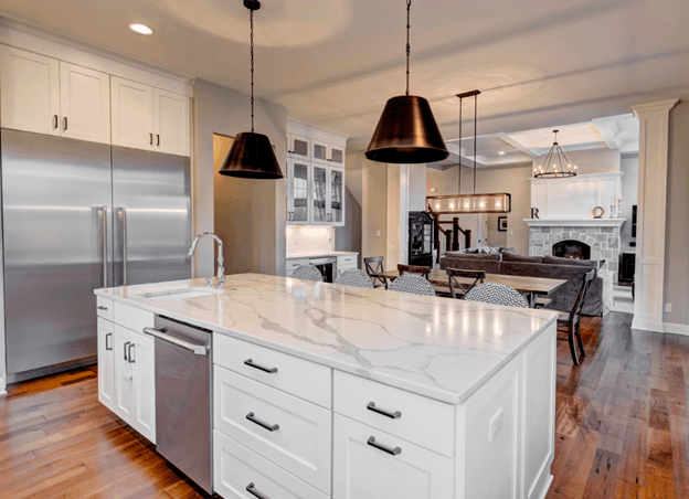 A kitchen with white cabinets , marble counter tops , stainless steel appliances and a large island.