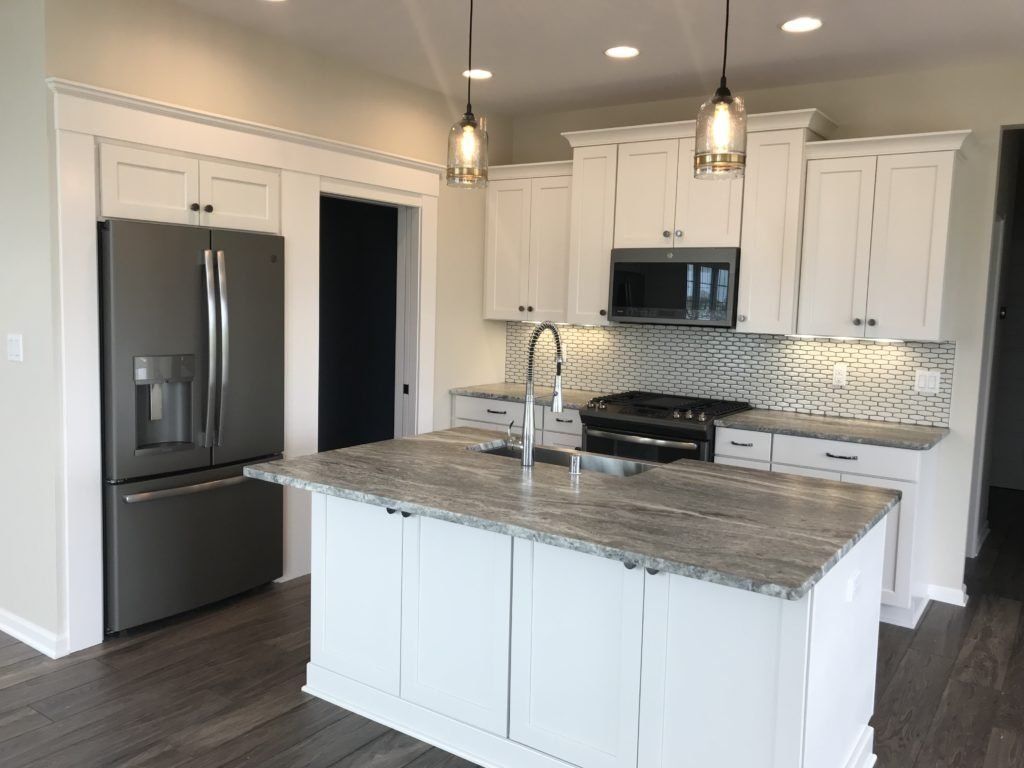 A kitchen with white cabinets , granite counter tops , stainless steel appliances and a large island.