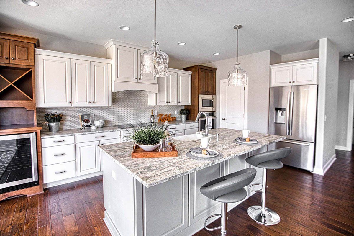A kitchen with white cabinets , granite counter tops , stainless steel appliances and hardwood floors.