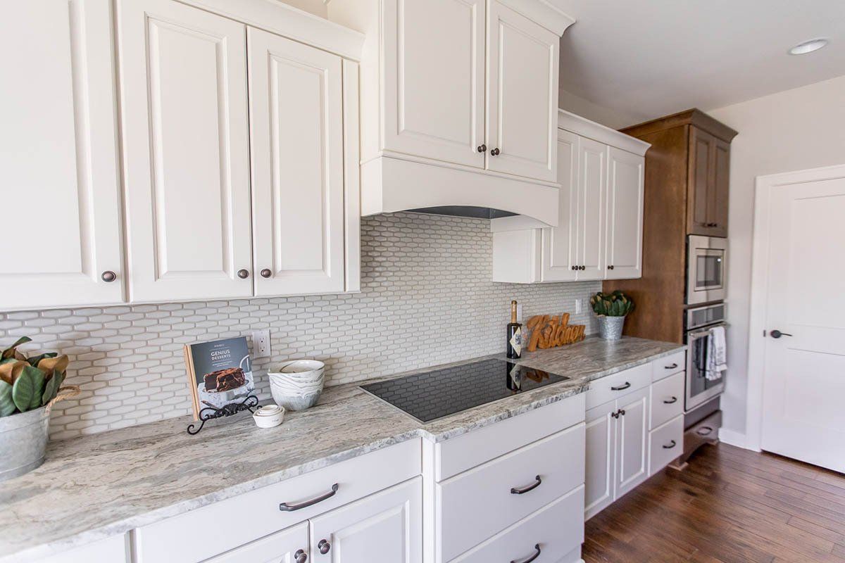 A kitchen with white cabinets , granite counter tops , and a stove top oven.