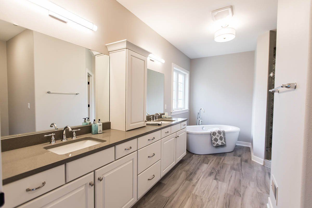 A bathroom with a tub , sink , mirror and cabinets.