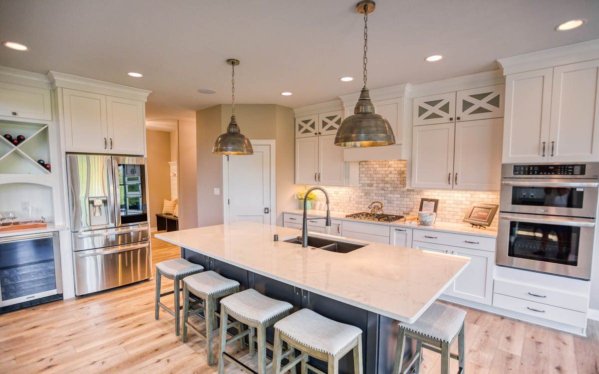 A kitchen with white cabinets , stainless steel appliances , a large island and stools.