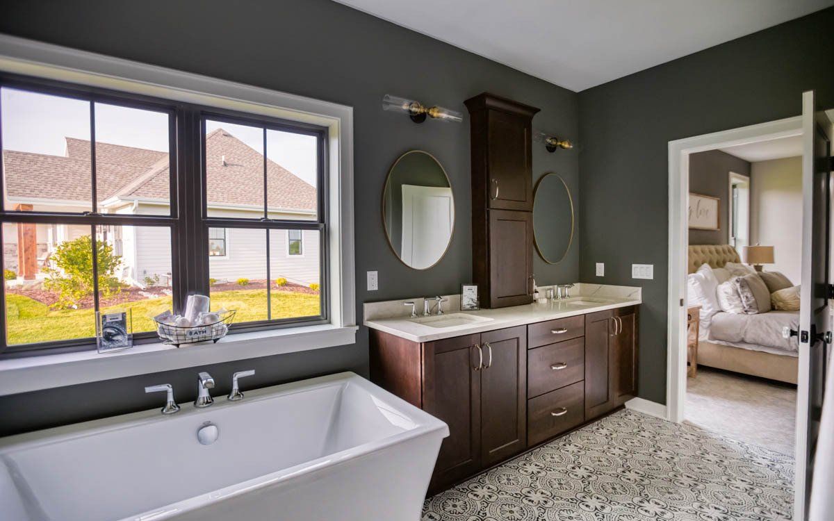A bathroom with a tub , sinks , mirrors and two windows.