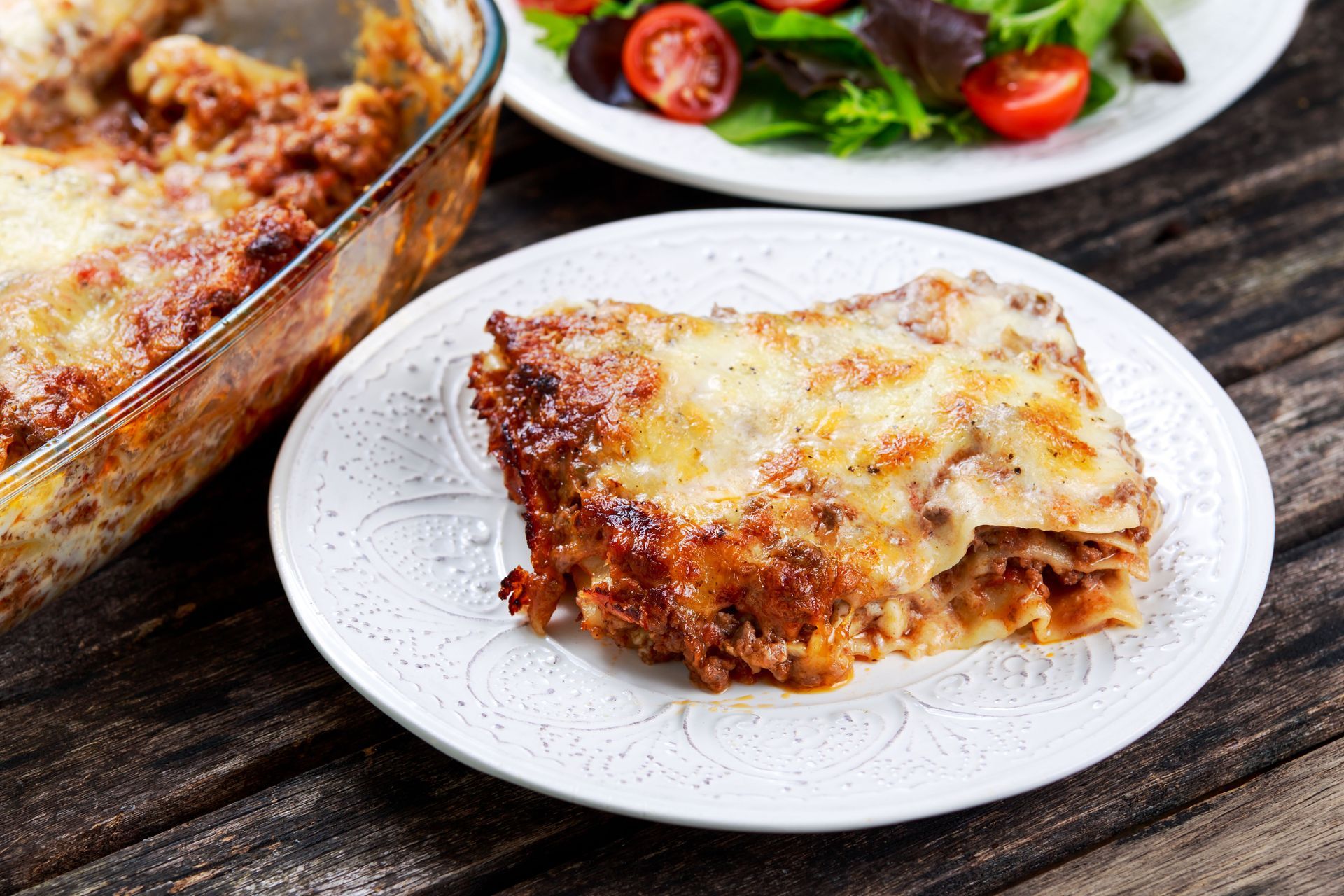 A slice of lasagna is on a white plate on a wooden table.