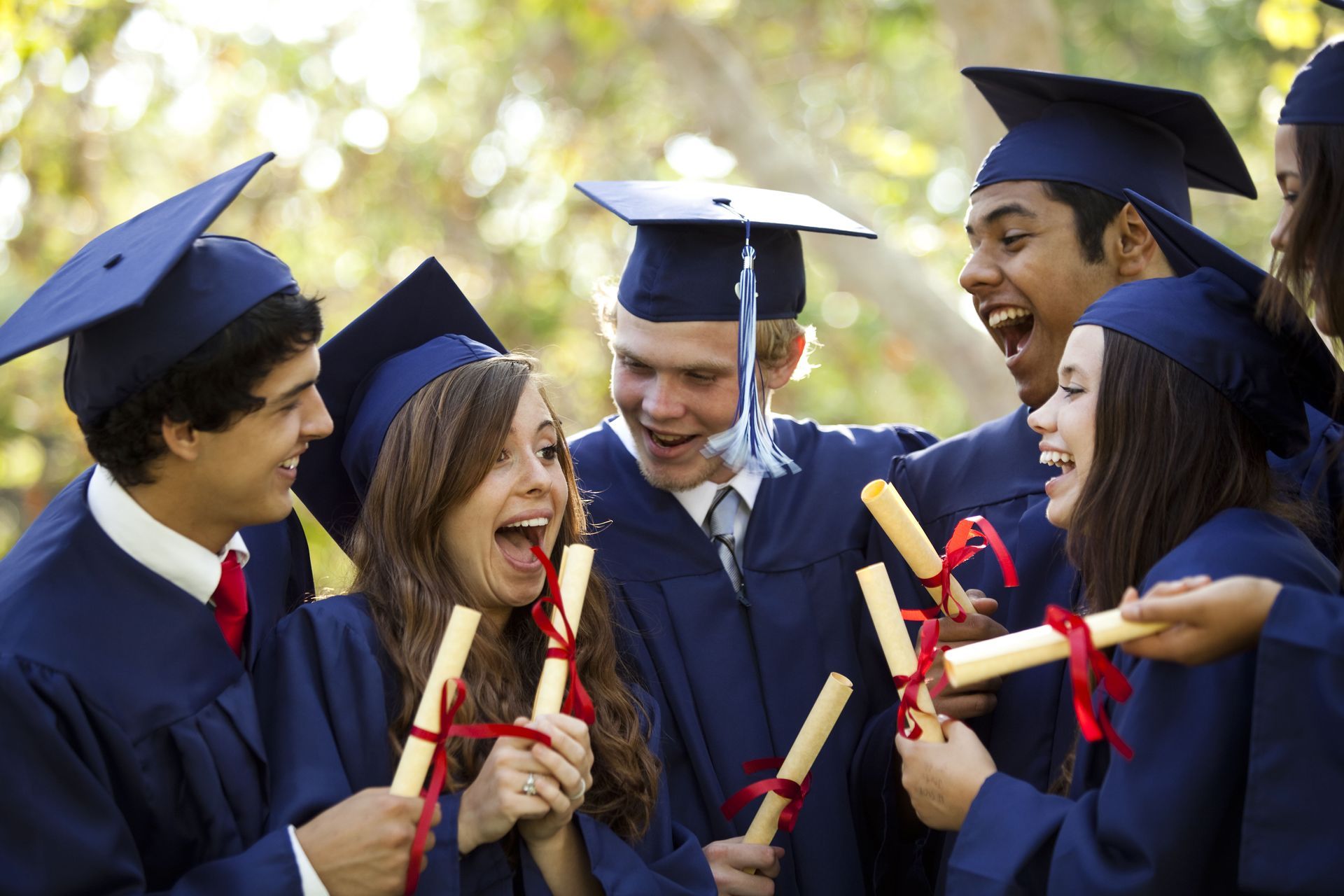 A group of graduates are holding their diplomas and laughing.