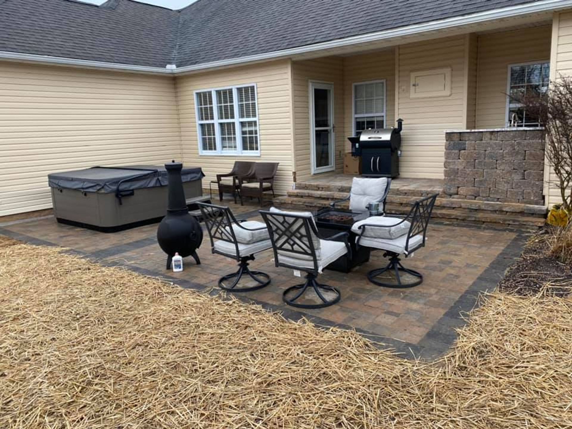 Patio with outdoor chairs, grill, and hot tub beside a beige house