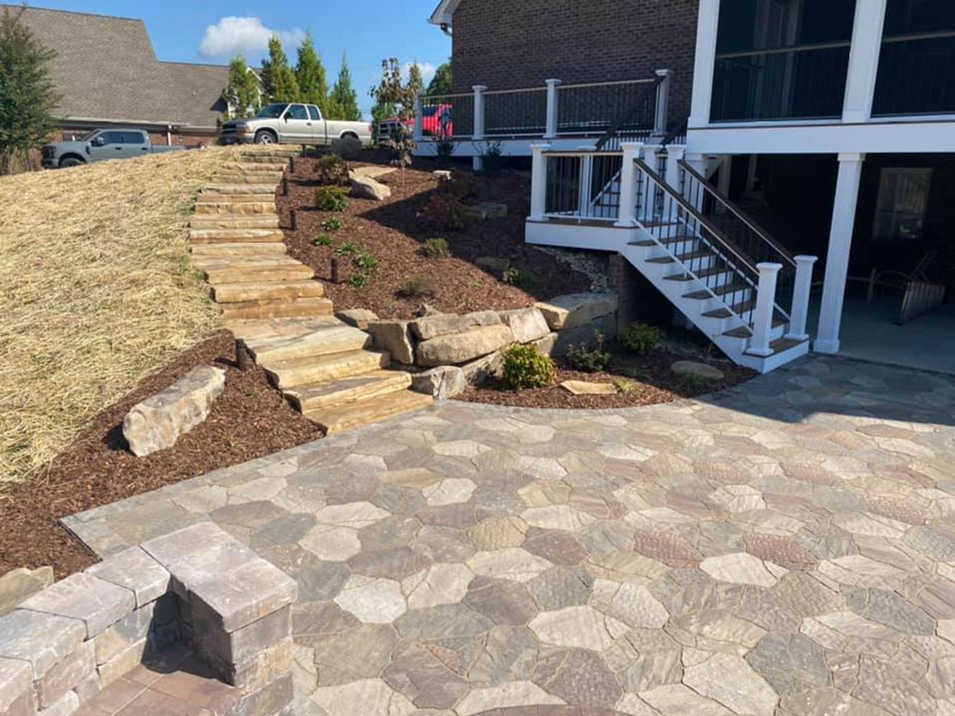 Stone steps and landscaped slope beside a house with a white porch and patio area