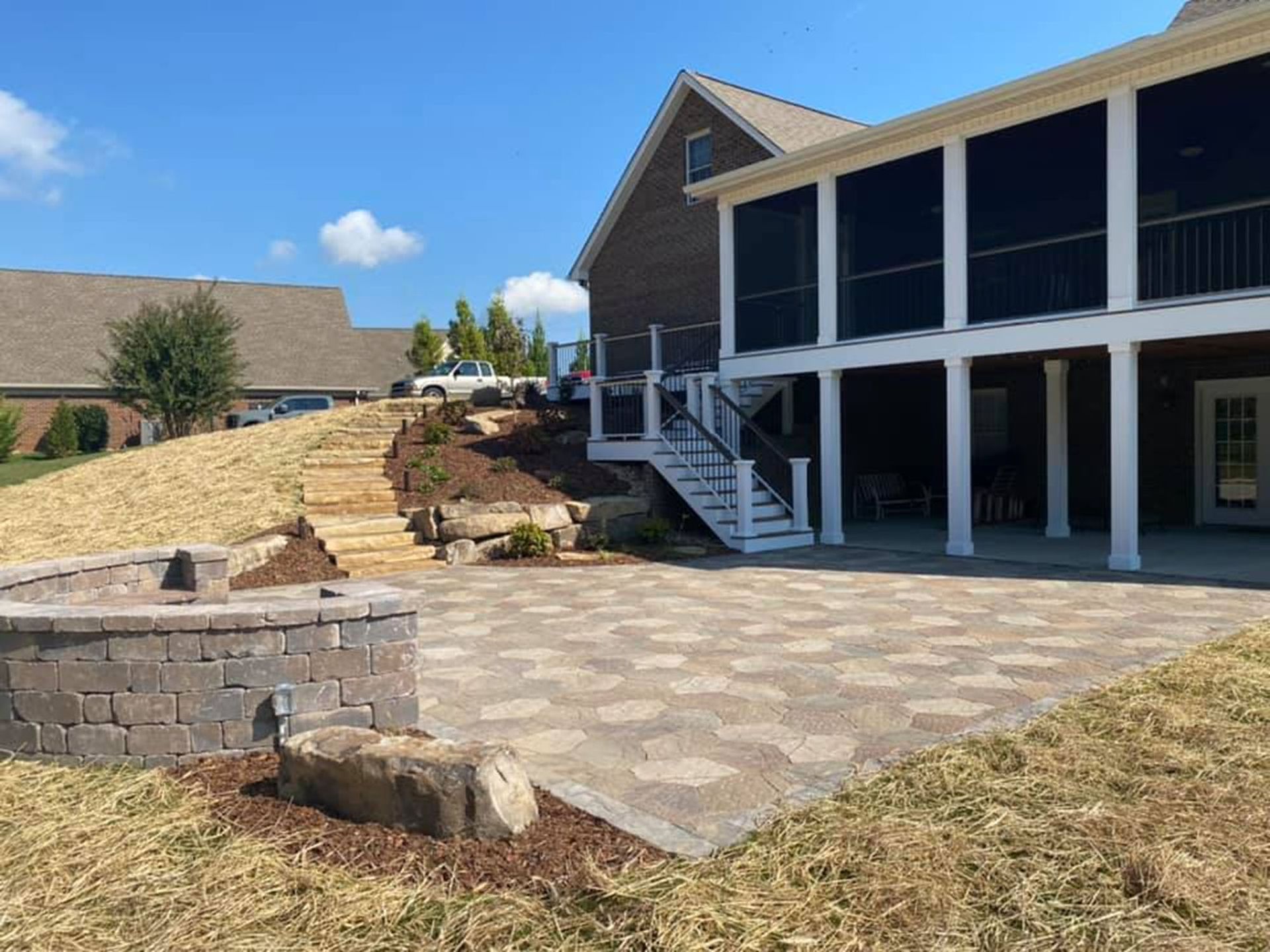 Backyard patio with stone pavers, retaining wall, stairs, and a screened porch under a blue sky