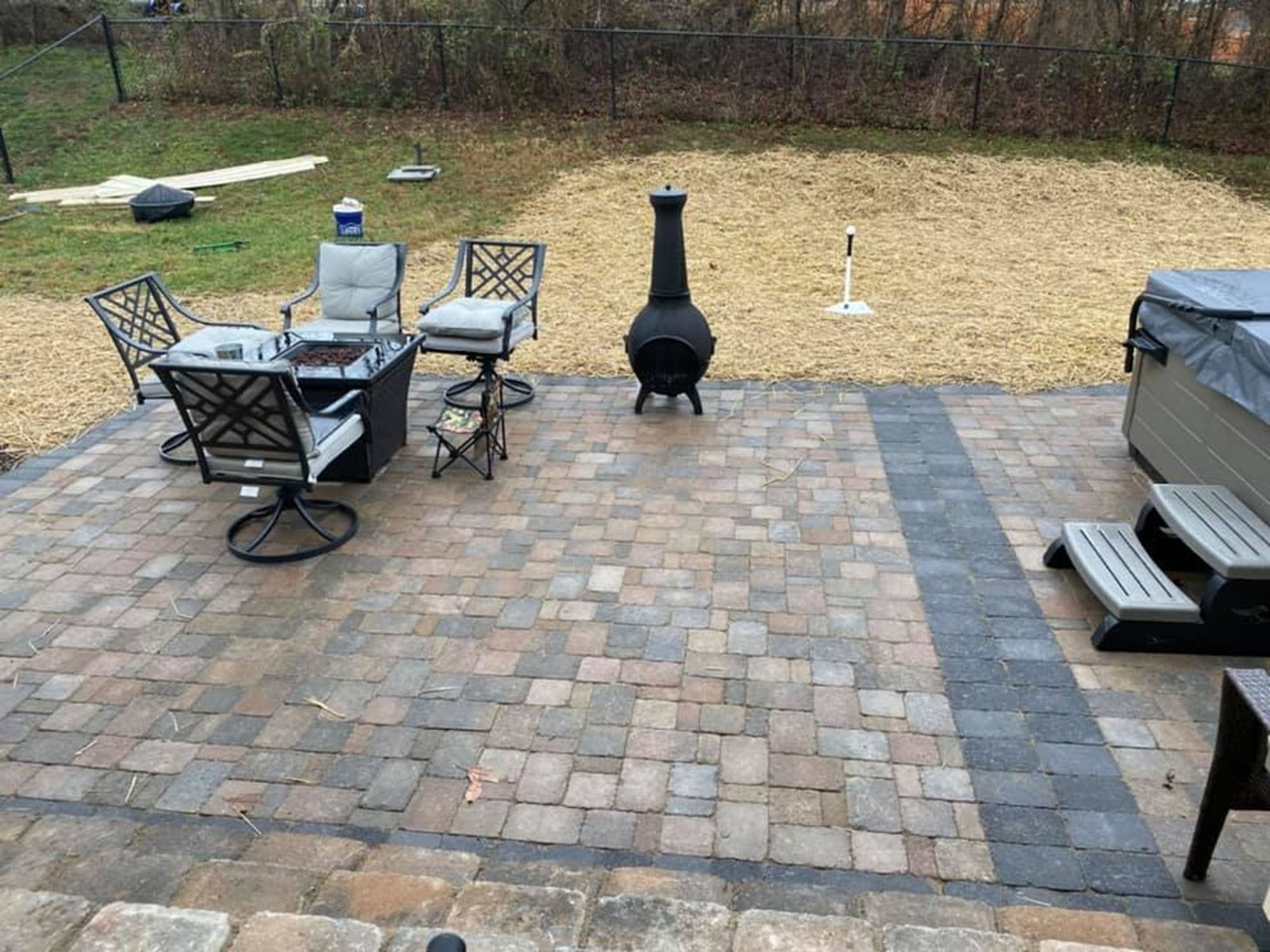Patio with outdoor dining table, chairs, fire pit, and grill on a paver patio with grassy yard beyond