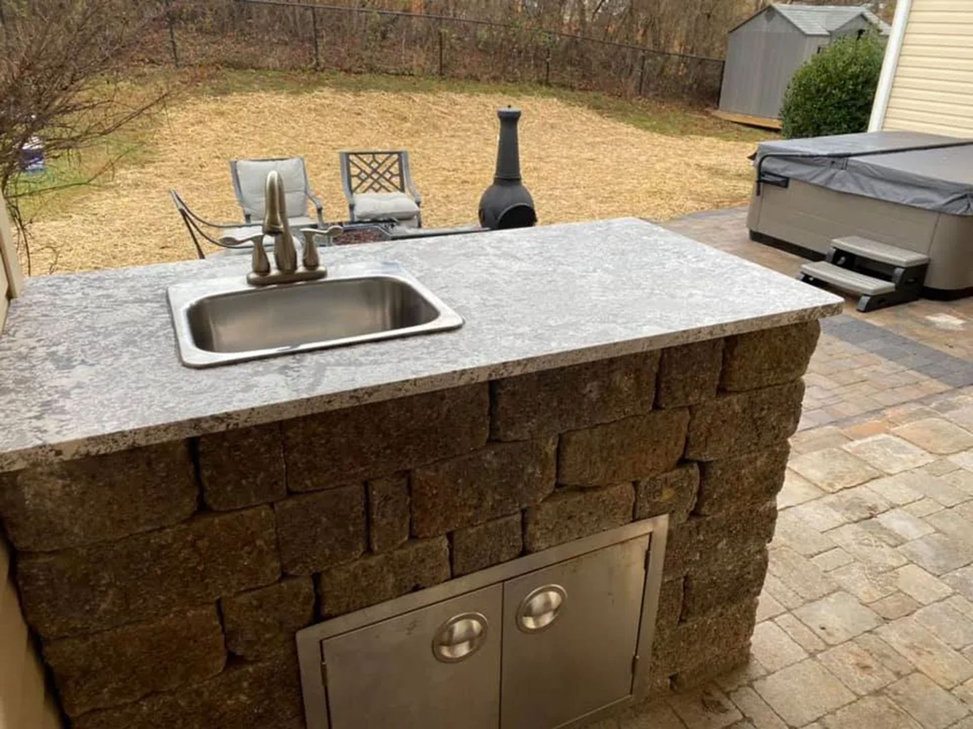 Outdoor stone patio sink with granite countertop, grill, and backyard view