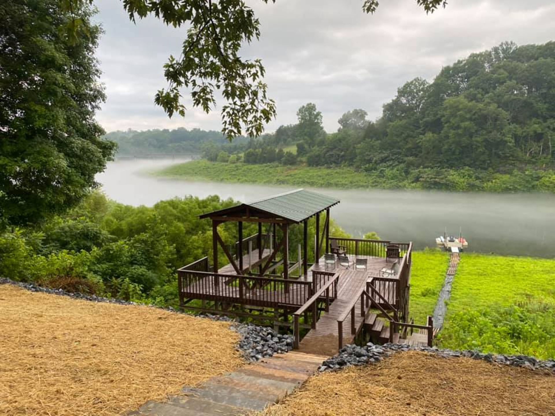 Wooden dock and pavilion by a calm lake, with green trees and misty water in the background