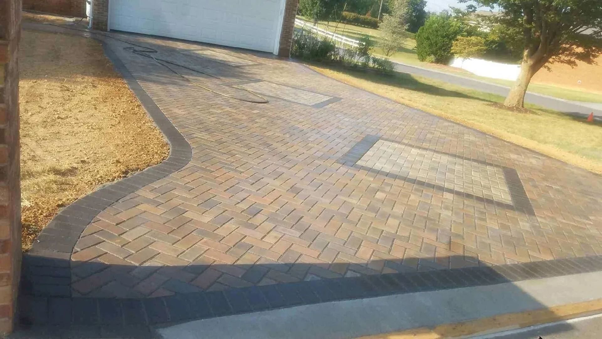Brick-paved driveway beside a garage, curving past two square utility covers in sunlight