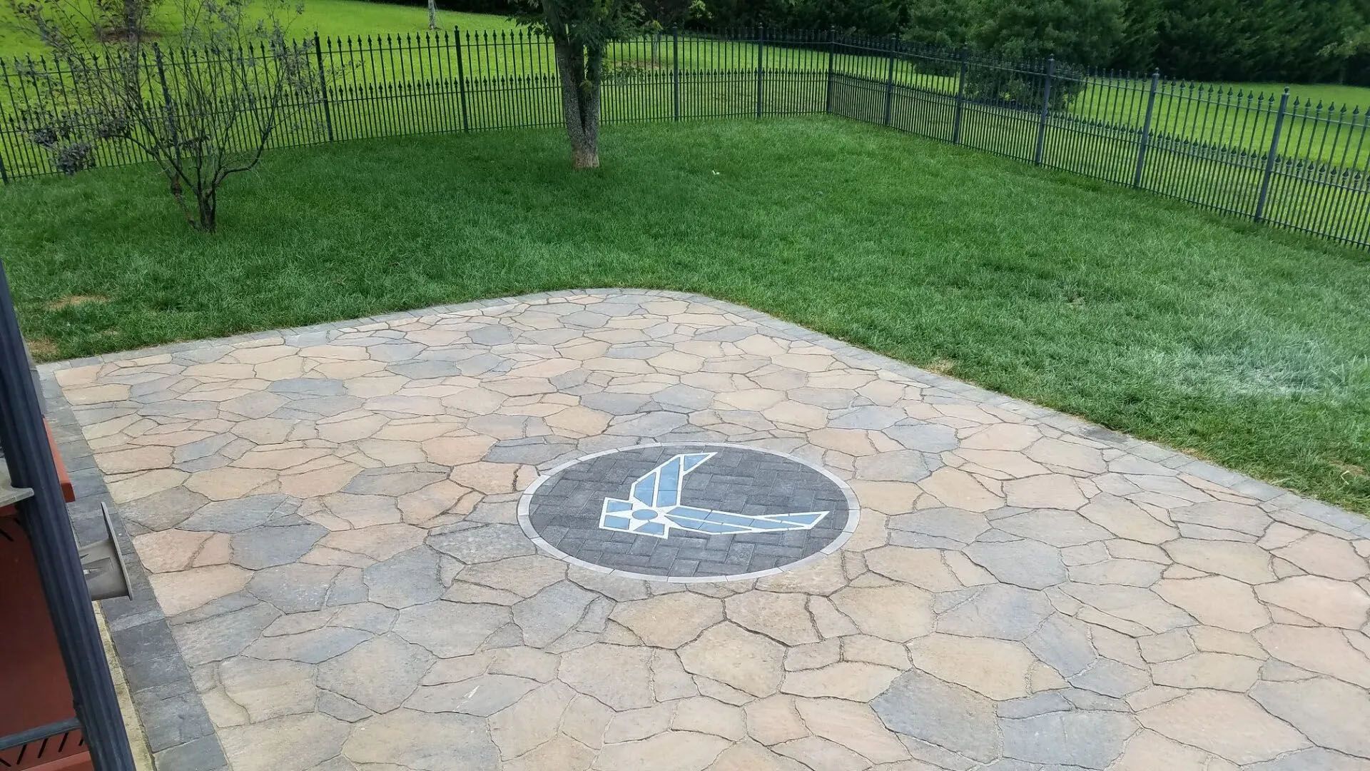 Stone patio with a circular fire pit, bordered by green grass and a fenced yard.