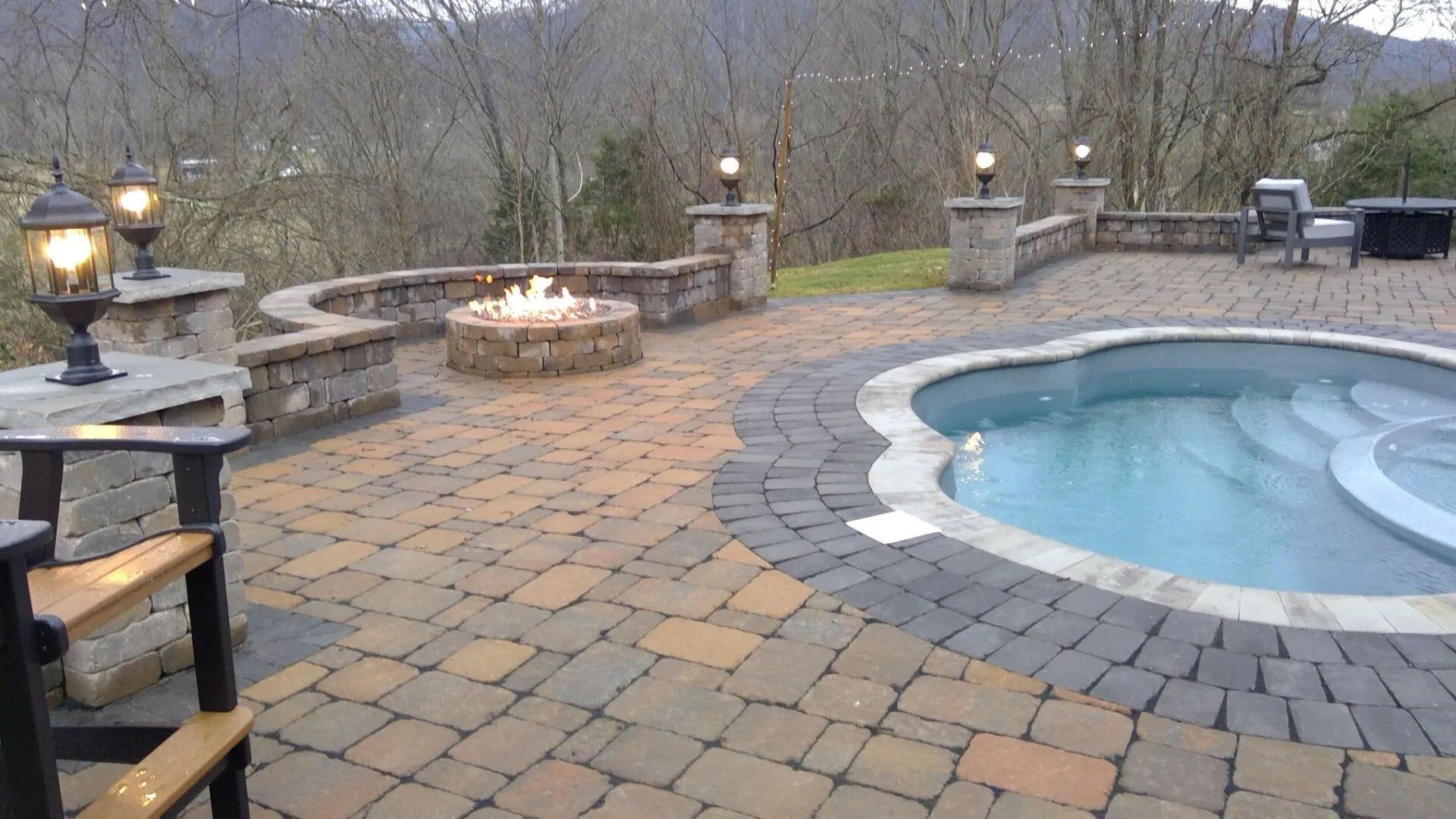Backyard patio with stone pavers, a hot tub, fire pit, and outdoor seating by bare trees