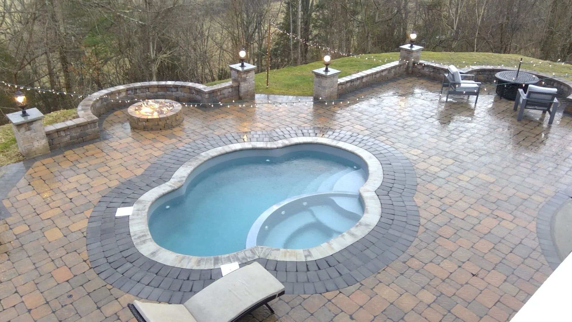 Small backyard patio with a kidney-shaped pool, wet brick pavers, and lounge chairs beside a stone wall