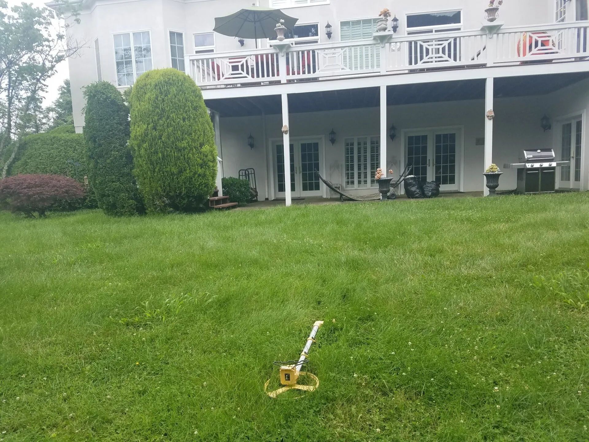 Lawn sprinkler on a green lawn in front of a white house with a covered patio