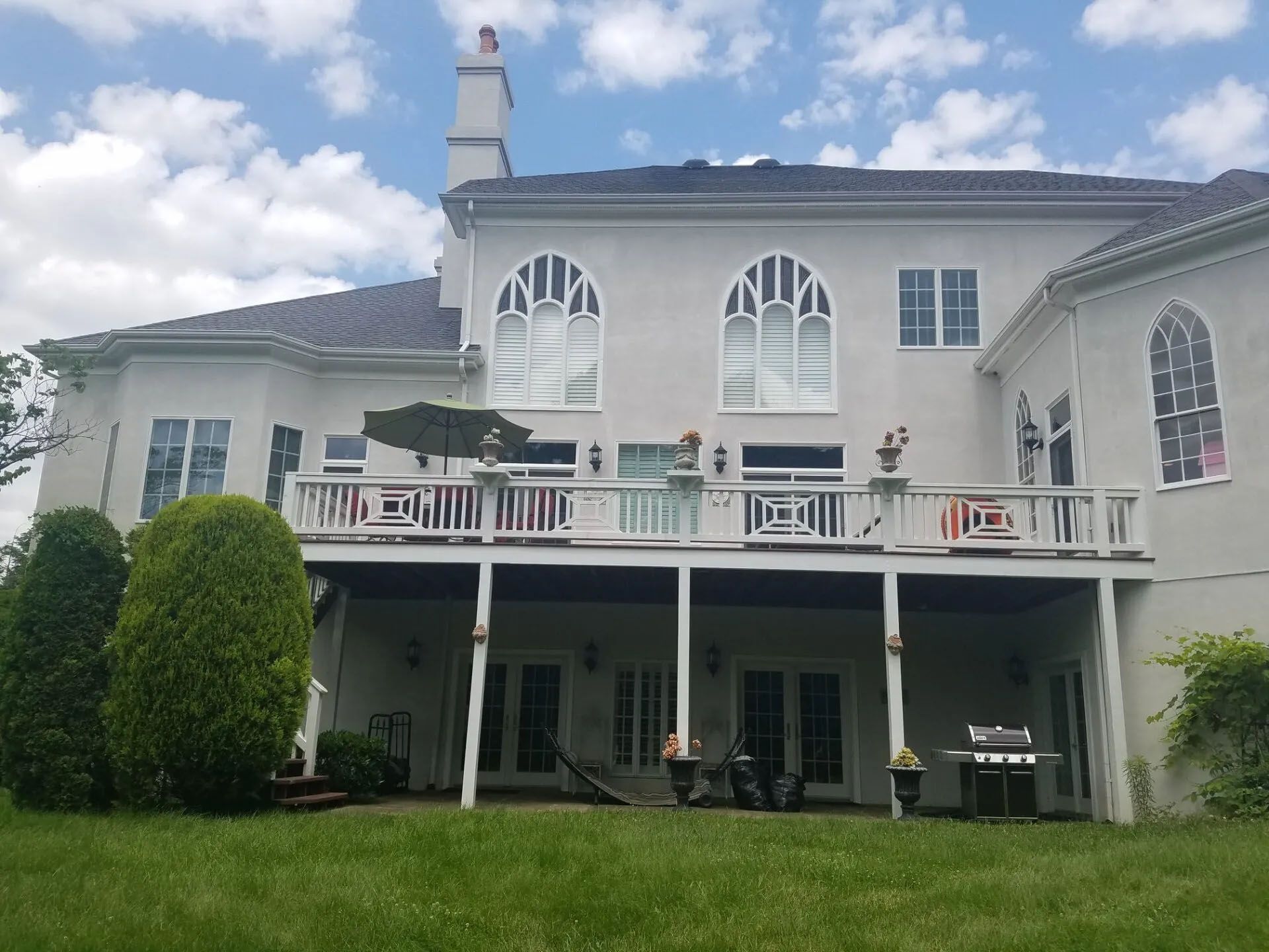 Large white two-story house with arched windows, balcony, and green lawn under a partly cloudy sky