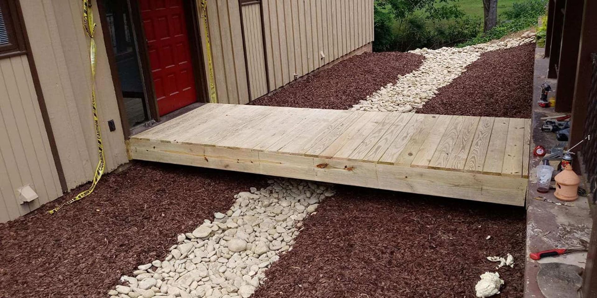 Wooden ramp over a gravel path leading to a red door beside a house