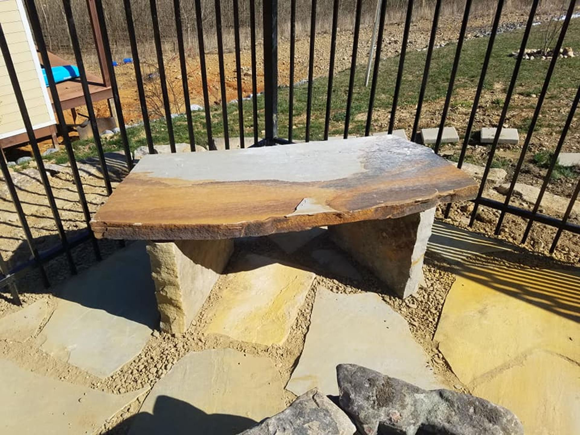 Weathered wooden bench with a dusting of snow, set in a fenced outdoor yard.