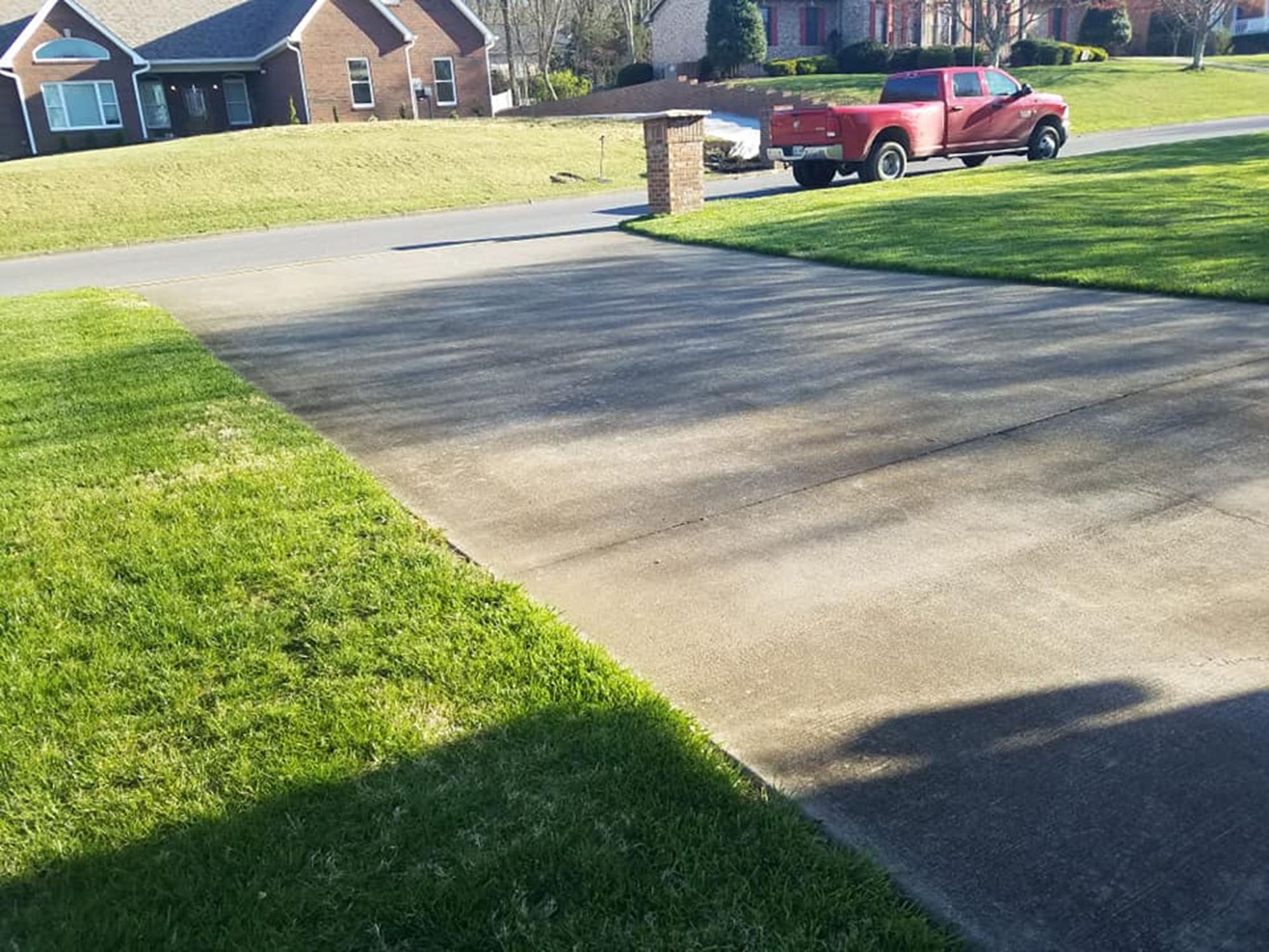 Suburban driveway with a red pickup truck, green lawn, and brick mailbox in bright sunlight