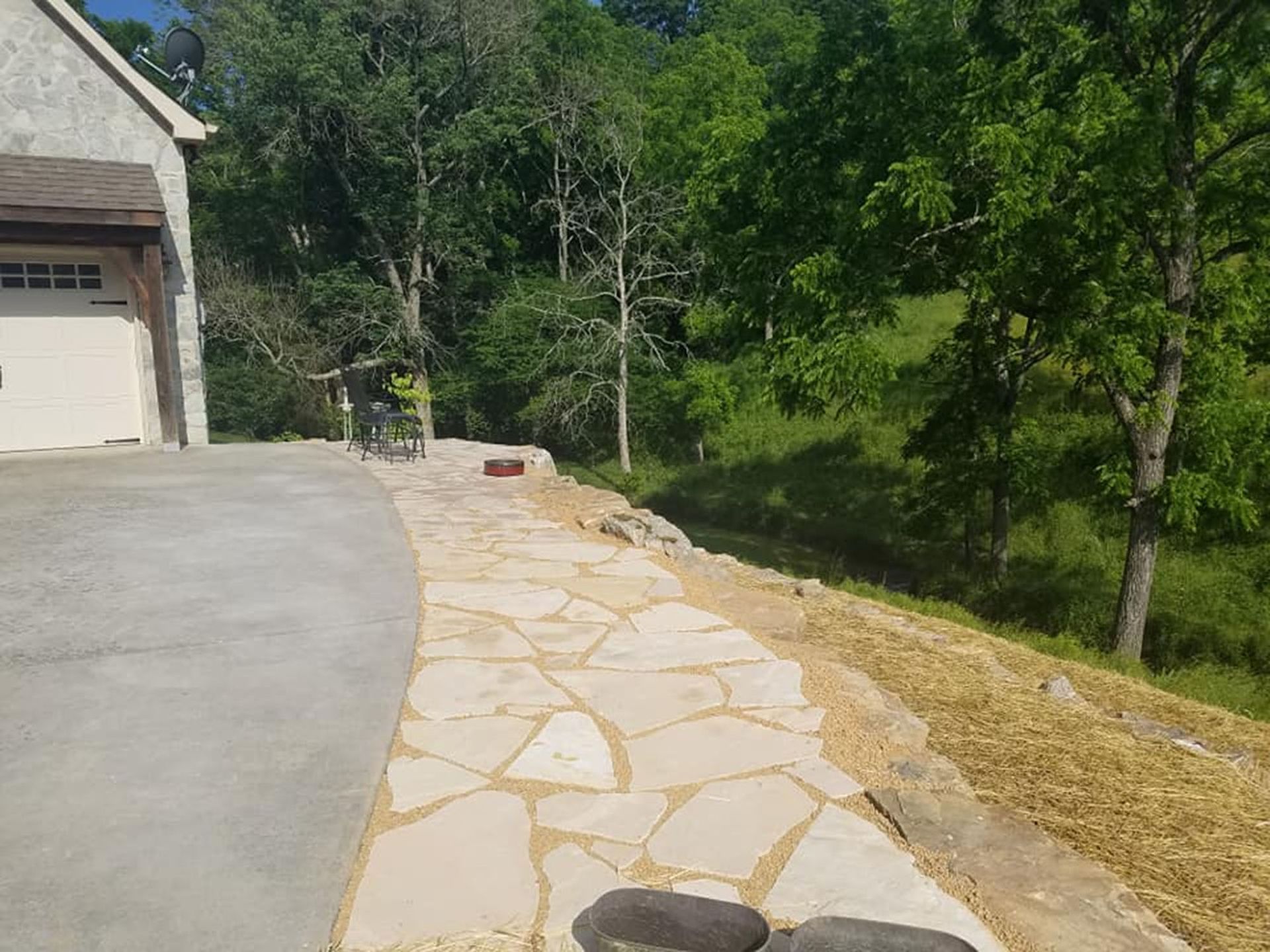 Driveway beside a house with a stone walkway leading past a wooded backyard.
