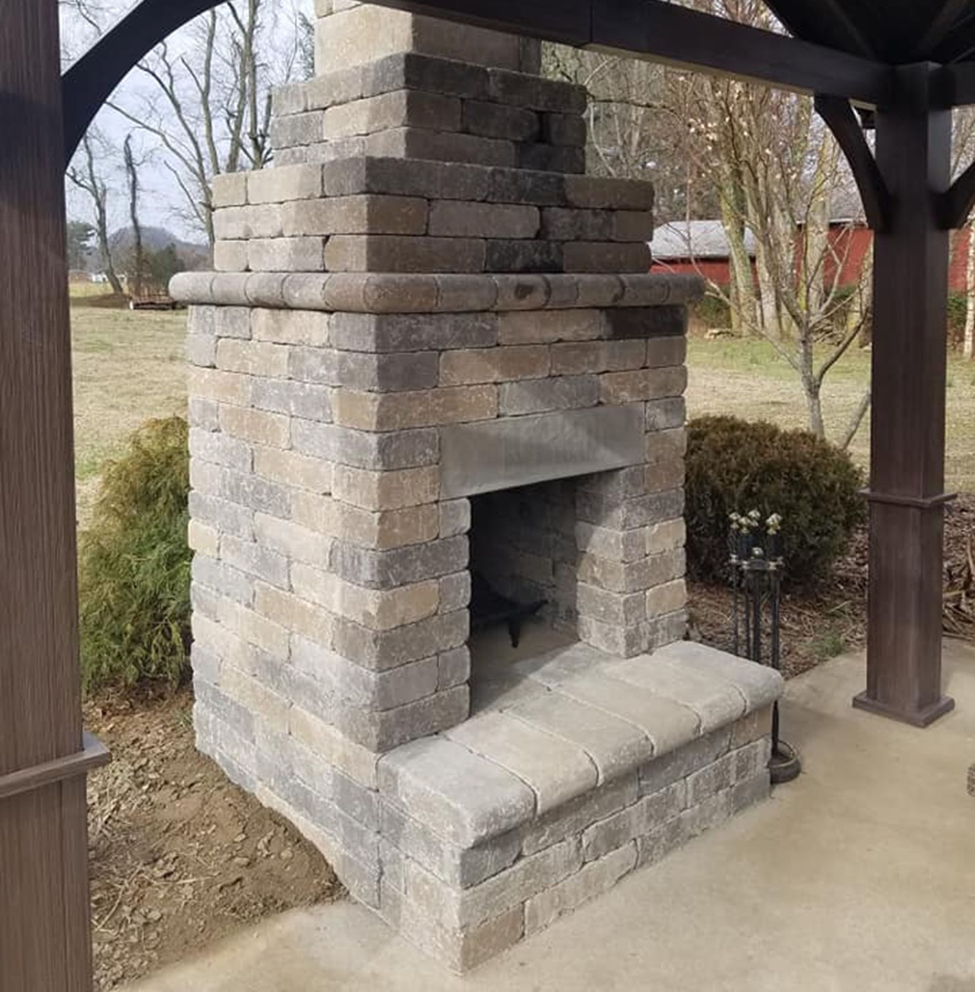 Brick outdoor fireplace under a wooden shelter on a concrete patio.