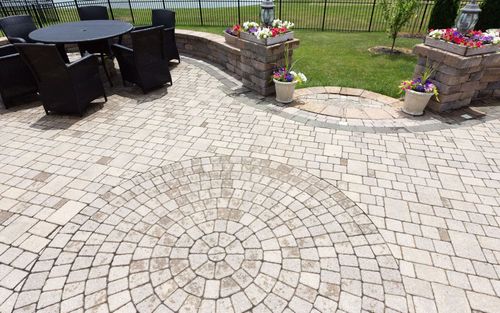 Patio with circular stone pavers, black wicker chairs, and flower planters by a grassy yard