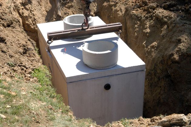 White utility tank installed in a dirt trench with a pipe and valve on top