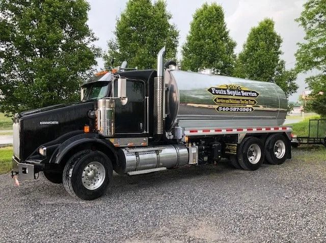 Black tanker truck parked on gravel, with chrome fuel tank and trees in the background
