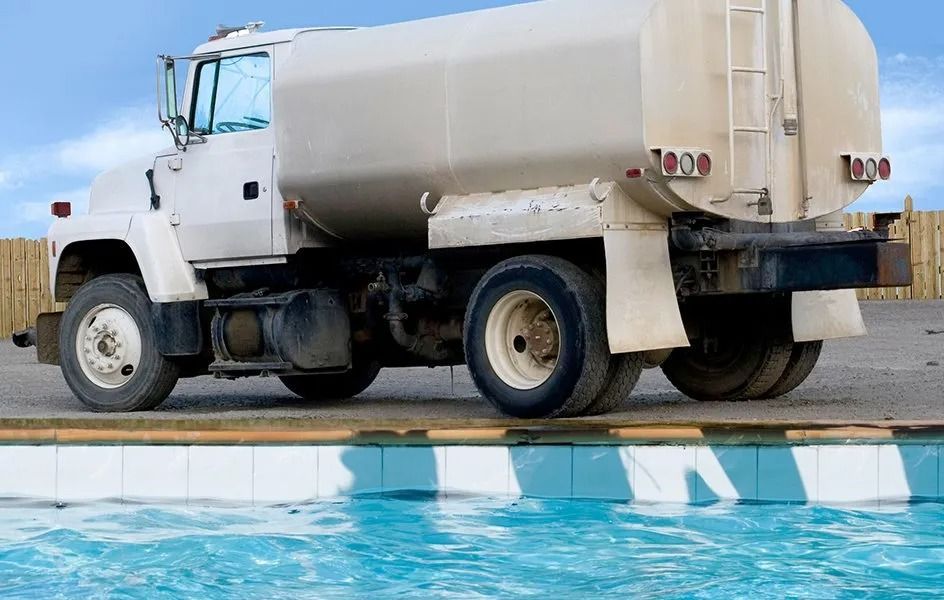 White tanker truck parked beside a blue swimming pool under a clear sky